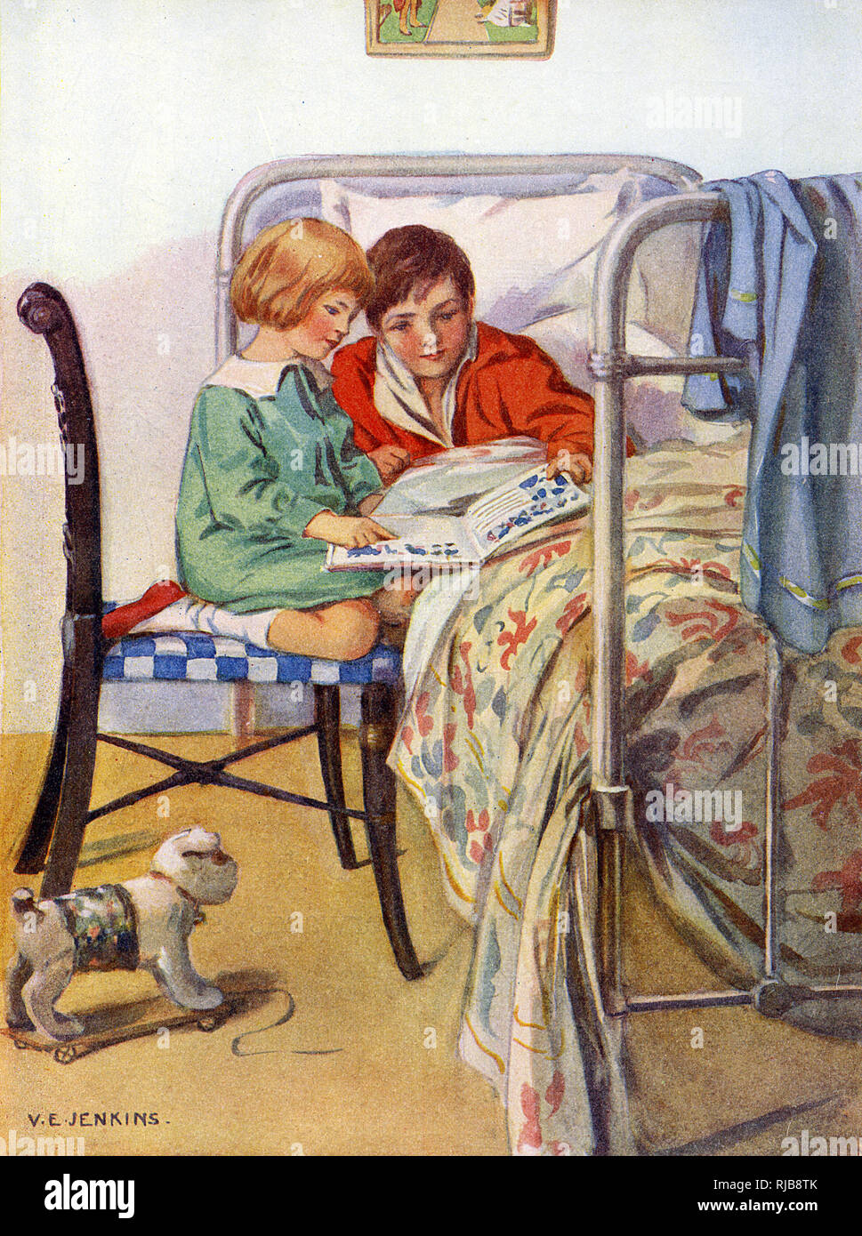 A little girl reads a book with an invalid friend who is recuperating in bed. Stock Photo