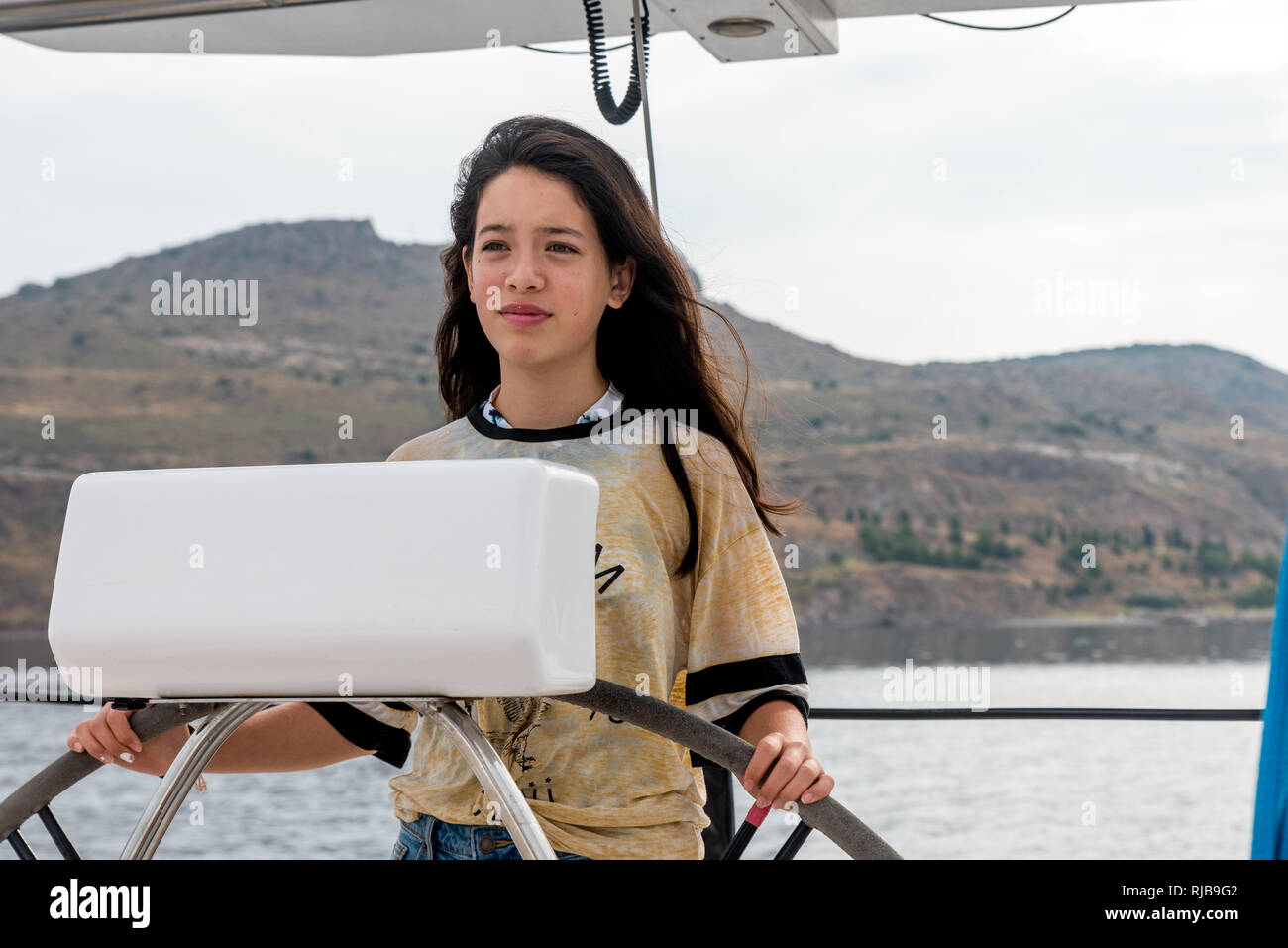 Young teen girl at he helm of a sailboat off the coast of Petra, Lesvos Stock Photo