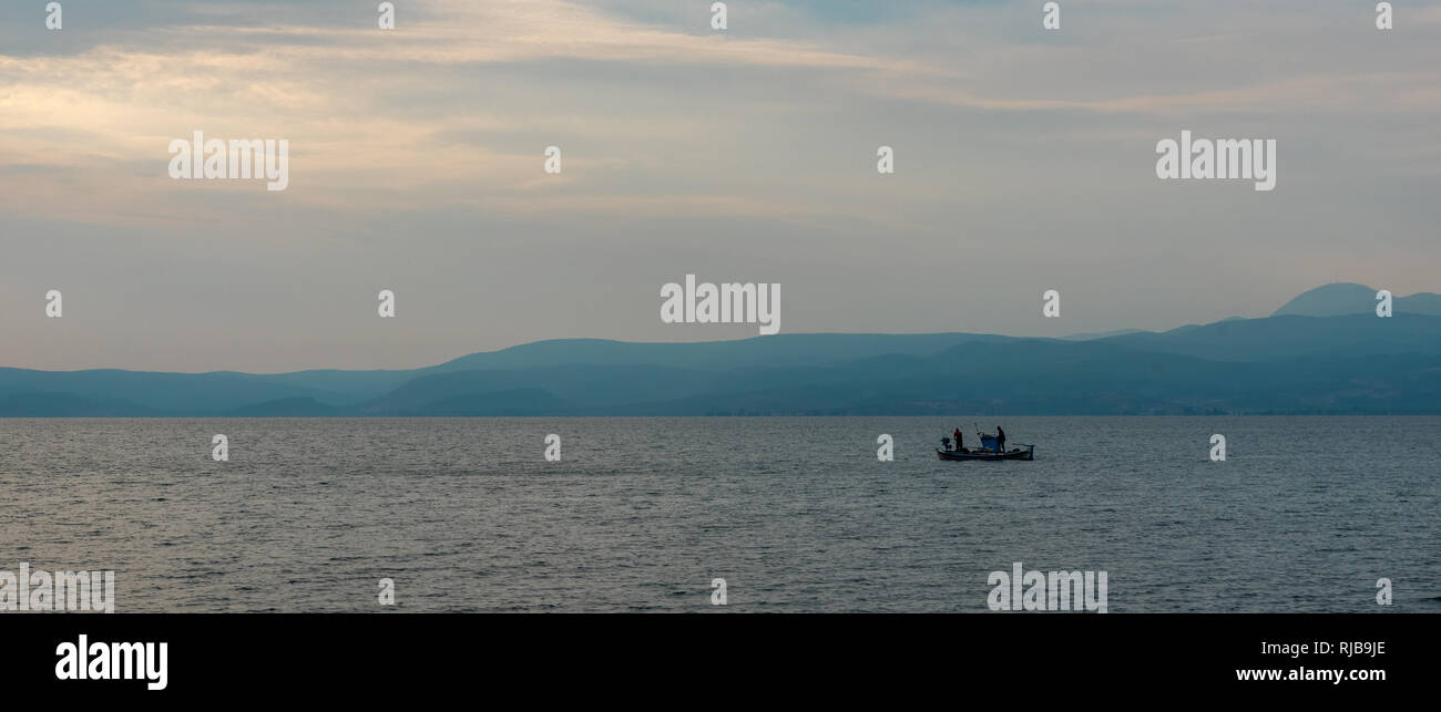 Two Greek fishermen on a boat in the sea with mountains in the background Stock Photo