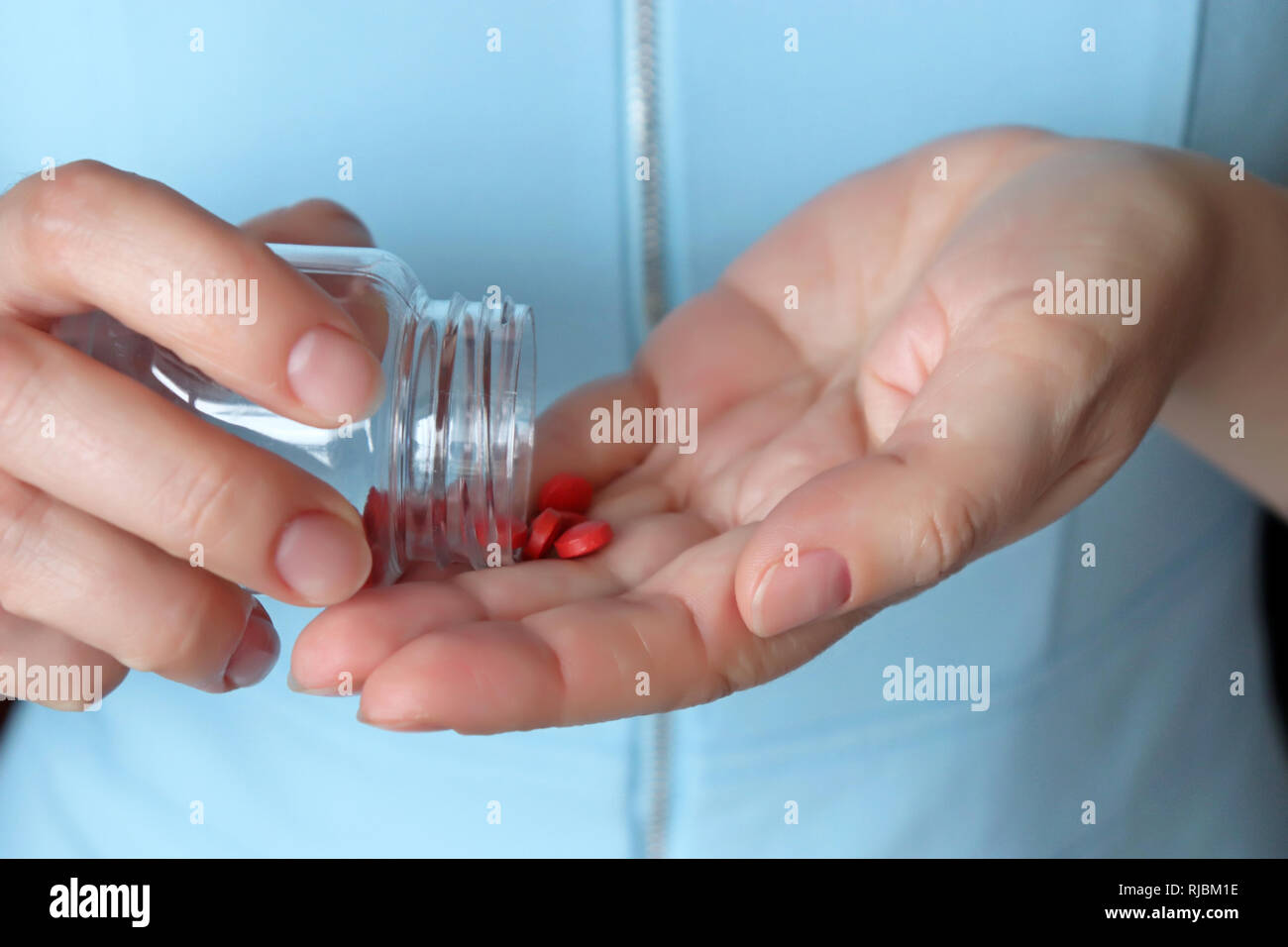 Woman taking pills, red tabs in female hands close-up. Concept of illness, vitamins, doctor with medication, contraceptive or diet Stock Photo