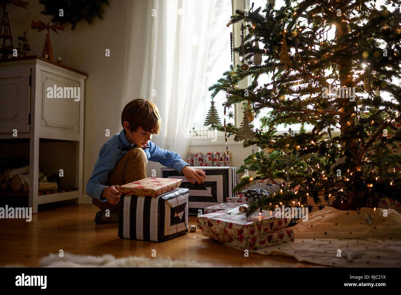 Boy kneeling in front of a Christmas tree looking at gifts Stock Photo