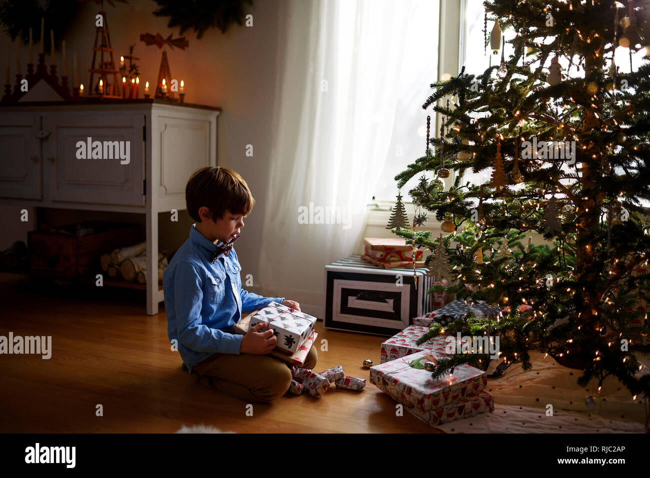 Boy sitting in front of a Christmas tree looking at gifts Stock Photo