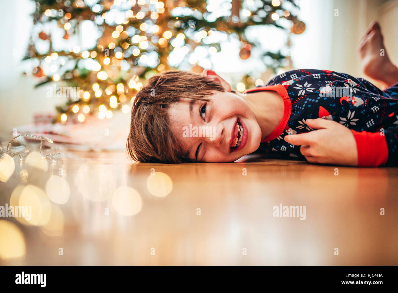 Boy lying on the floor in front of a Christmas tree laughing Stock Photo