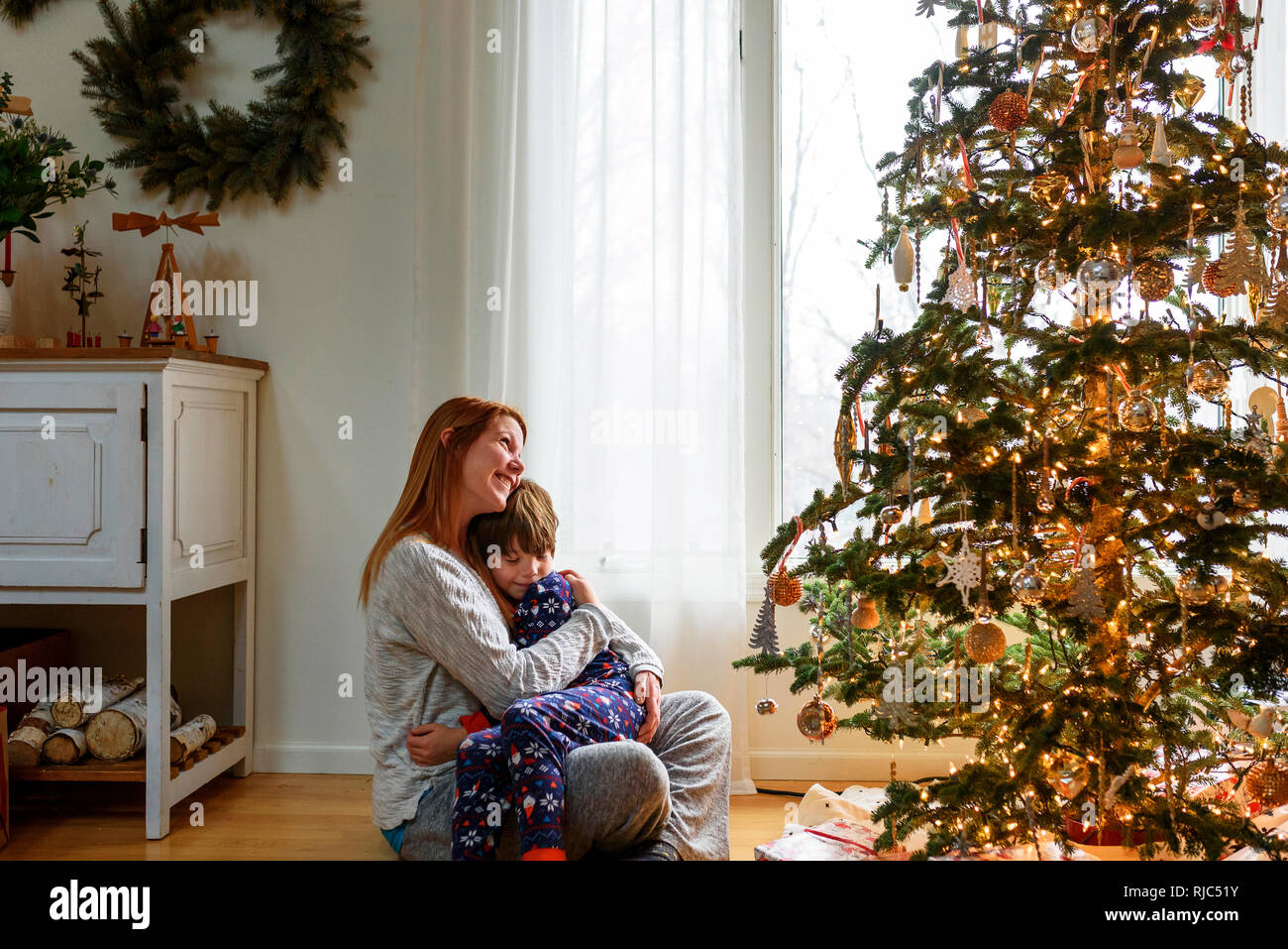 Woman sitting by a Christmas tree hugging her son Stock Photo