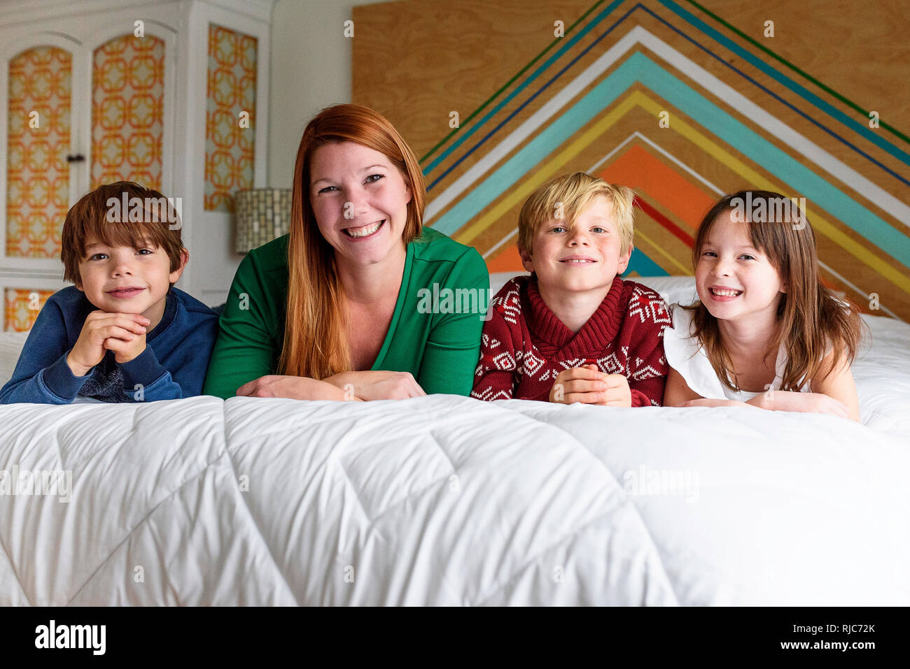 Mother and her three children lying on a bed smiling Stock Photo
