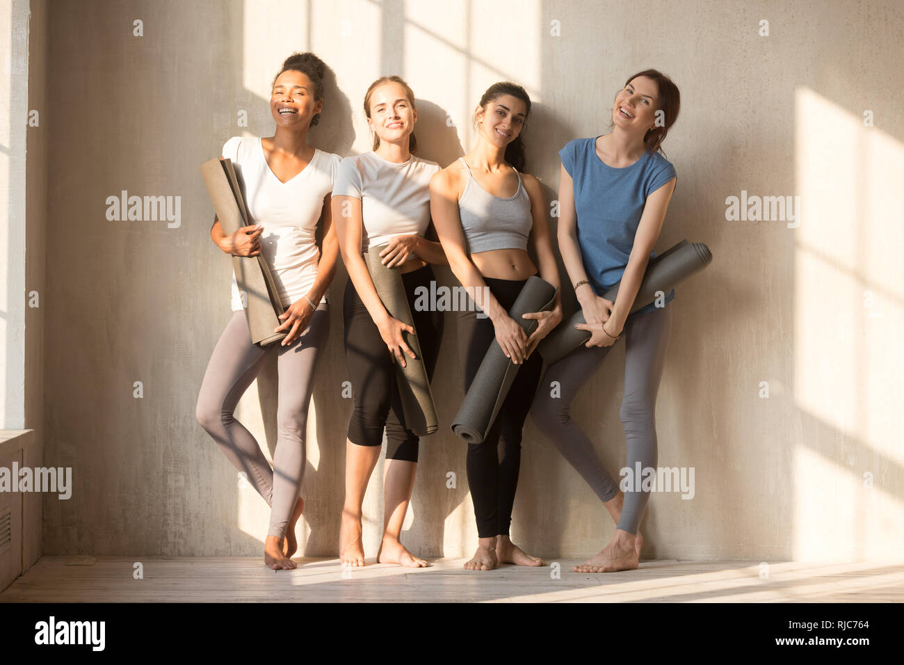 Smiling multiracial girls pose with yoga mats waiting for training Stock Photo