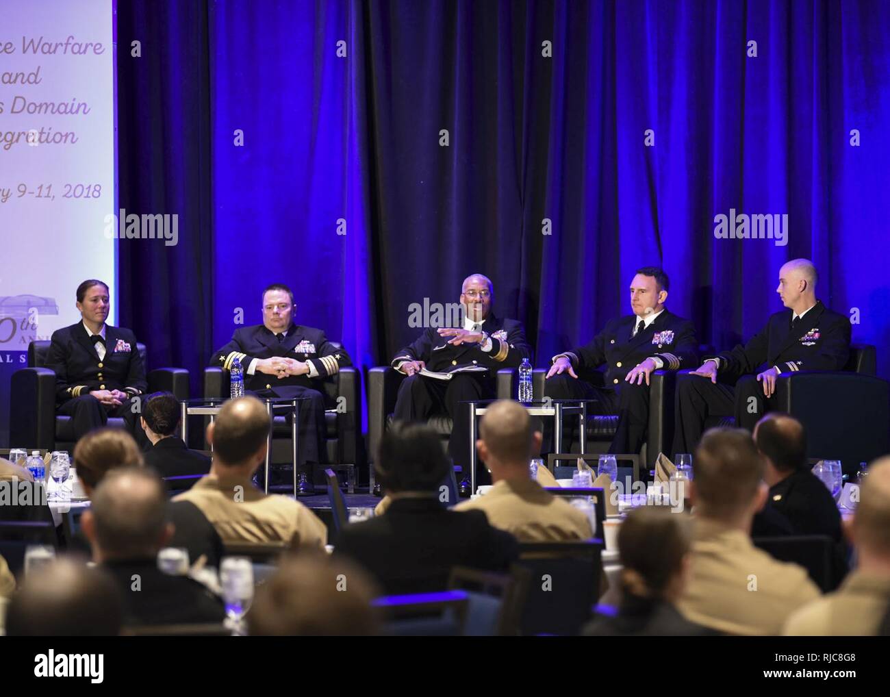 CRYSTAL CITY, Va. (Jan. 09, 2018) Rear Adm. Jesse A. Wilson Jr., commander, Naval Surface Force Atlantic, middle, Capt. Scott Robertson, commander, Surface Warfare Officer School, middle right, and Capt. Rick Cheeseman, head, Surface Officer Distribution Division, middle left, speak to officers during a junior officer roundtable discussion at the Surface Navy Association’s 30th National Symposium. Also serving as a panelist are Lt. Cmdr. Katie Whitman, left, and Lt. James Lewis, right.  This year's symposium focuses on 'Surface Forces and Cross-Domain Integration,' highlighting common procedur Stock Photo