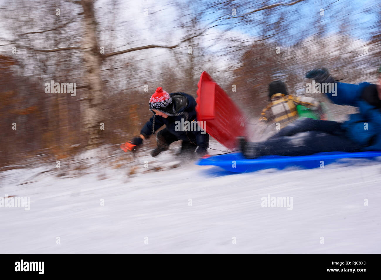Three children falling off their sledges, Wisconsin, United States Stock Photo
