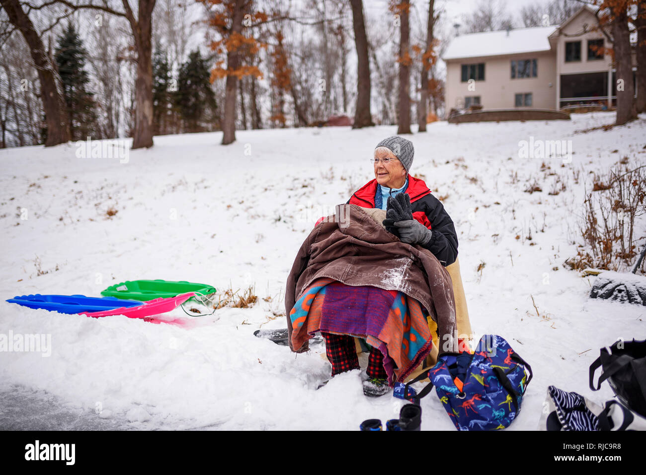 Grandmother sitting outdoors watching her grandchildren sledging, Wisconsin, United States Stock Photo