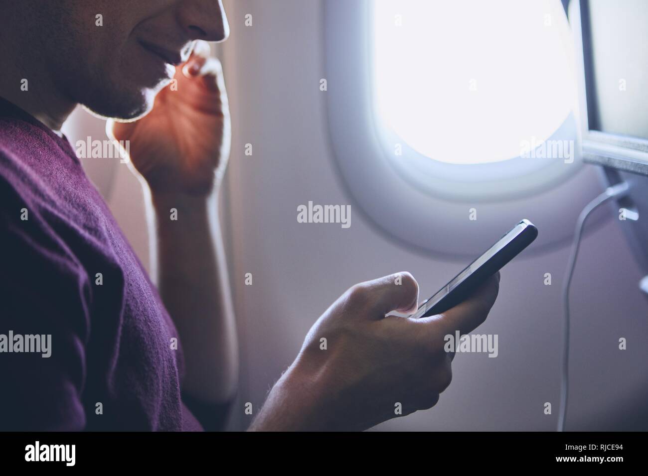 Connection during flight. Young man using mobile phone in airplane. Stock Photo
