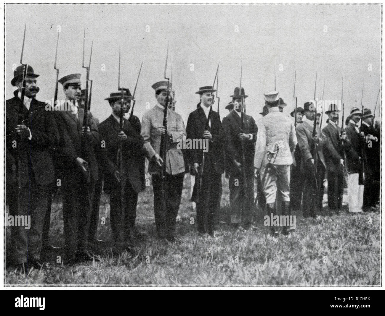 A line of men both in uniform and in civilian clothing hold up rifles with bayonets attached. Stock Photo