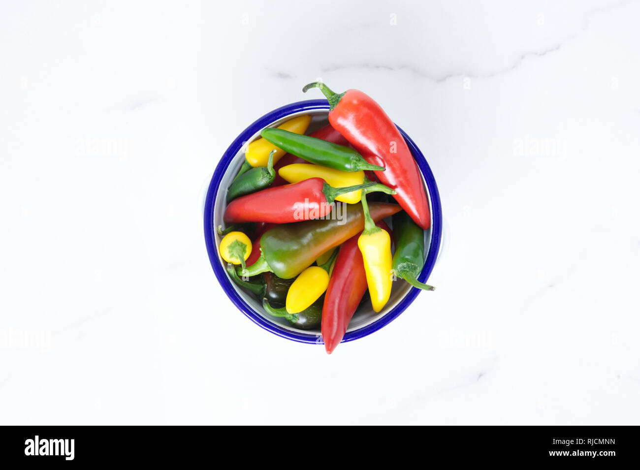 Capsicum annuum. Chillies in an enamel bowl on a marble surface. Stock Photo