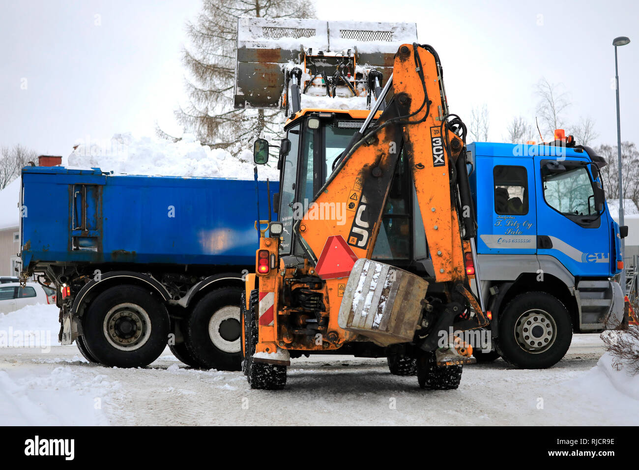 Salo, Finland - February 2, 2019: JCB loader loads snow onto blue Sisu dump truck trailer to be transported to a snow dumping area. Stock Photo