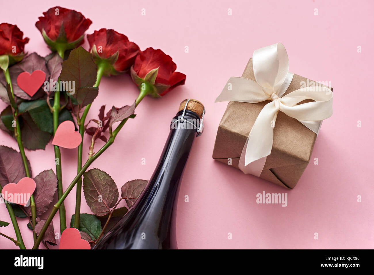 Surprise for her. Special gift box with white ribbon, red roses and champagne on pink background Stock Photo