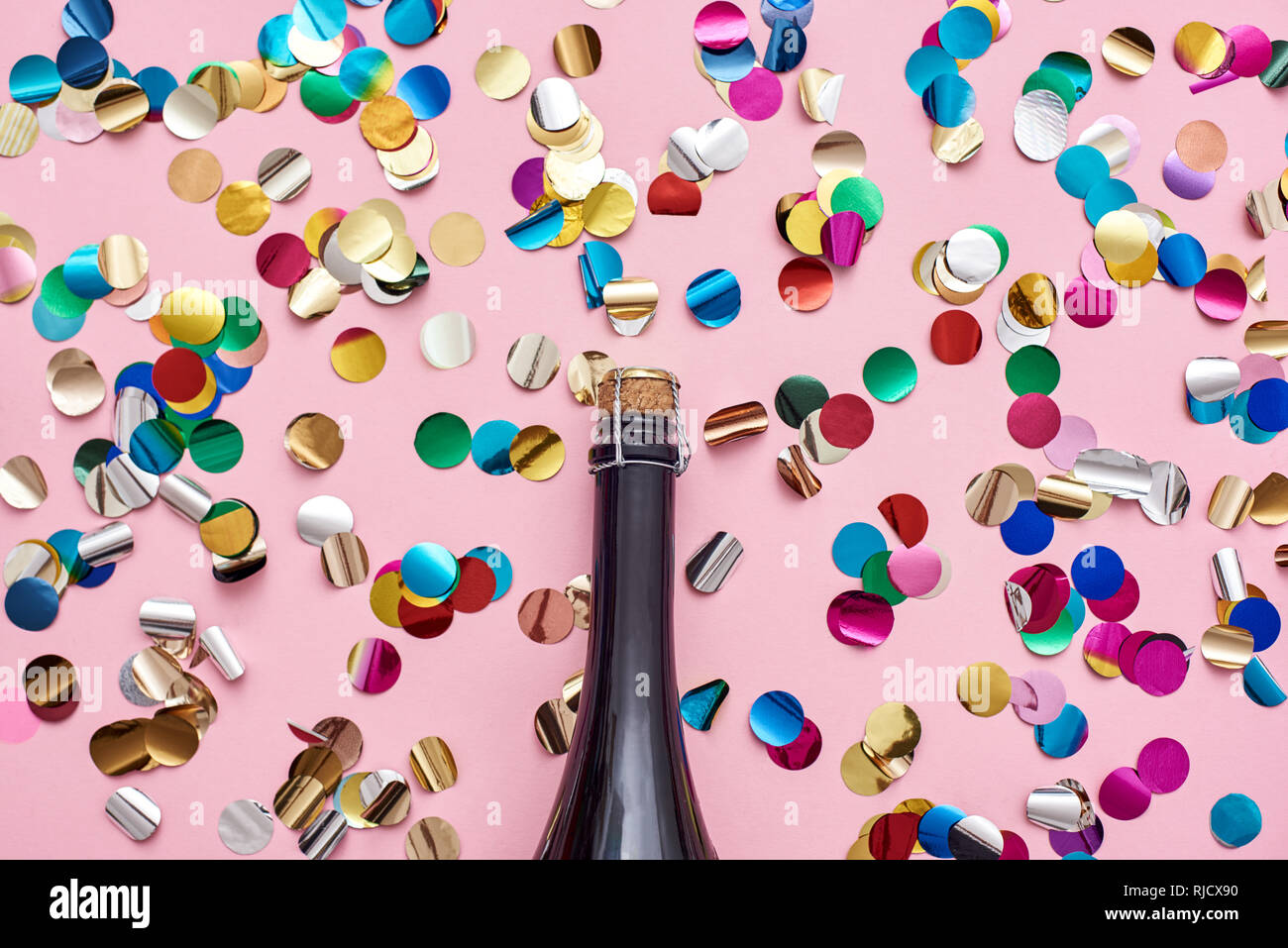 Party started A bottle of champagne on pink background with glittering confetti. Top view Stock Photo