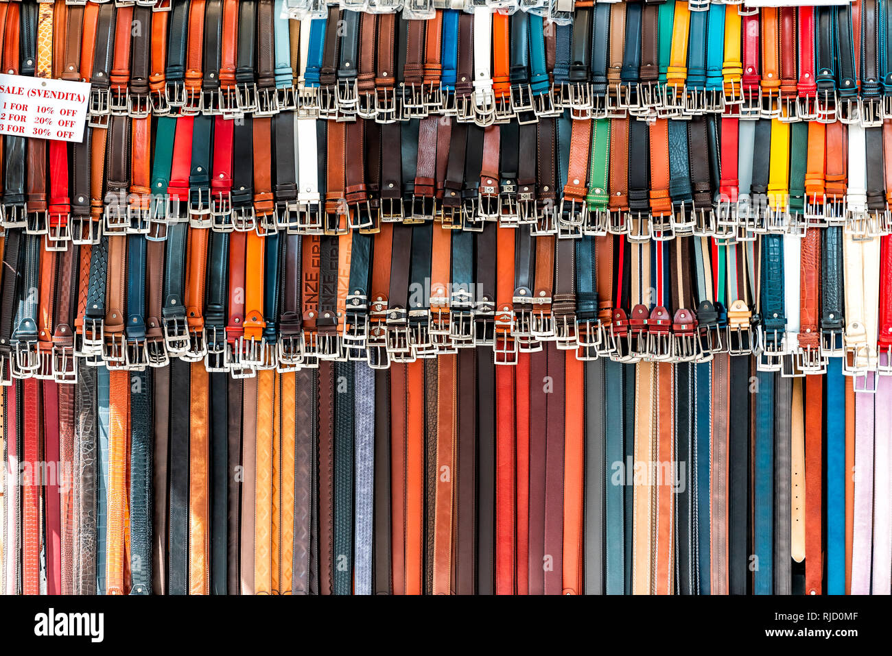 Florence, Italy - August 30, 2018: Closeup pattern of many belts leather colorful vibrant colors hanging on display with sale sign in shopping street  Stock Photo