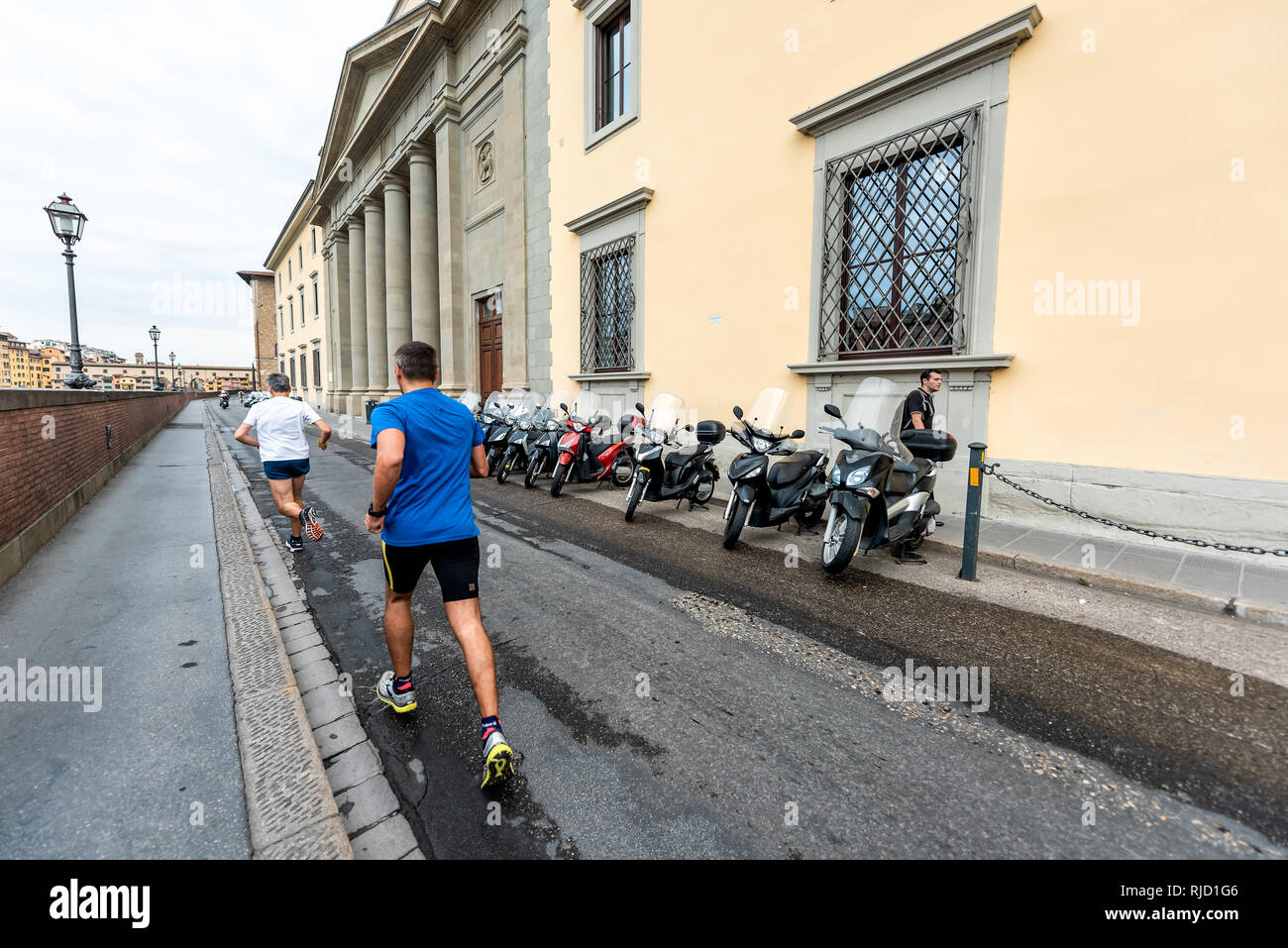 Florence, Italy - August 31, 2018: Firenze orange yellow colorful buildings by Arno river during summer morning in Tuscany with men running jogging on Stock Photo