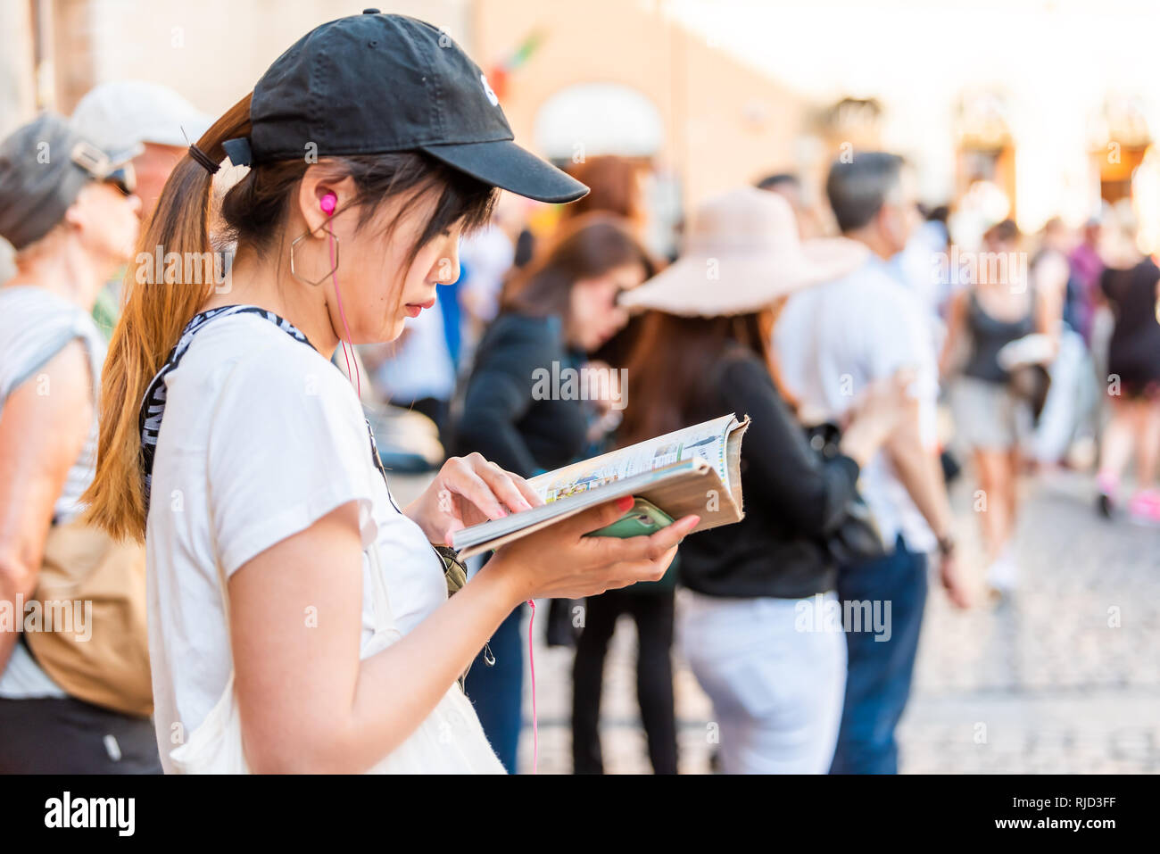 Rome, Italy - September 4, 2018: Closeup profile portrait of young Asian woman on street in historic city by Trevi fountain reading guide book Stock Photo