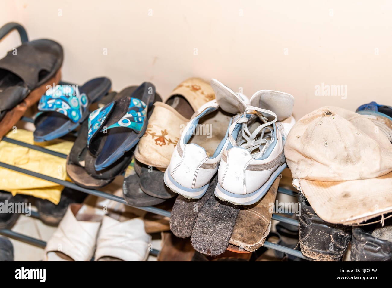 Many pairs of shoes on display on shelf rack with dirty soiled hat in rustic cottage farm house home dacha closeup Stock Photo