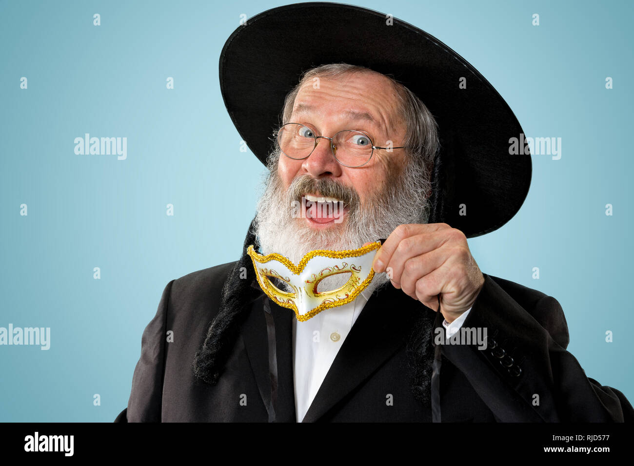 Portrait of a senior orthodox Hasdim Jewish man with wooden Grager Ratchet at Jewish festival of Purim at studio. The purim, jewish, festival, holiday, celebration, judaism, pastry, tradition, cookie, religion concept. Stock Photo