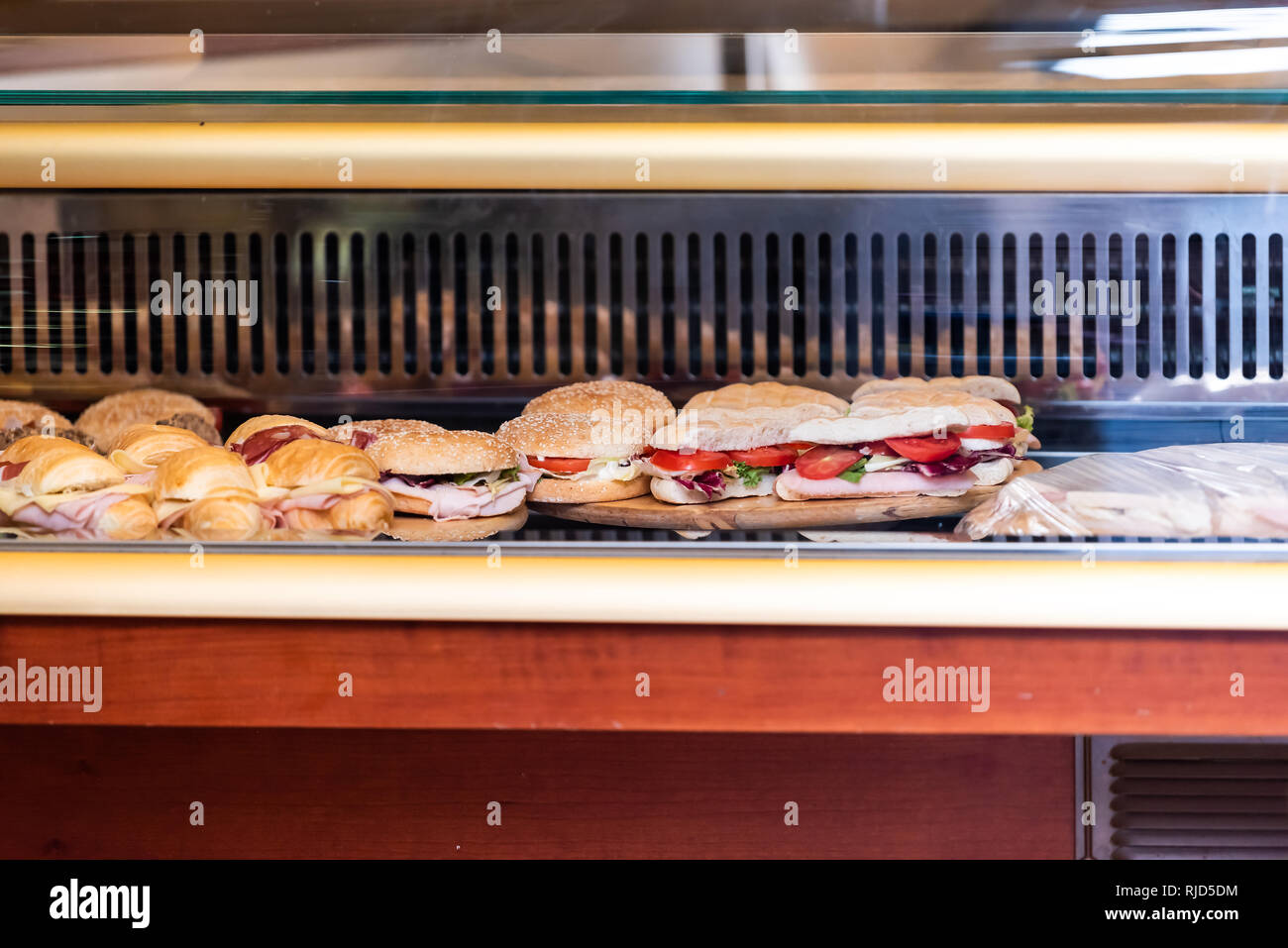 Display of many large sandwiches behind glass window of store stuffed with ham cheese and tomatoes in Italy with croissants and buns Stock Photo