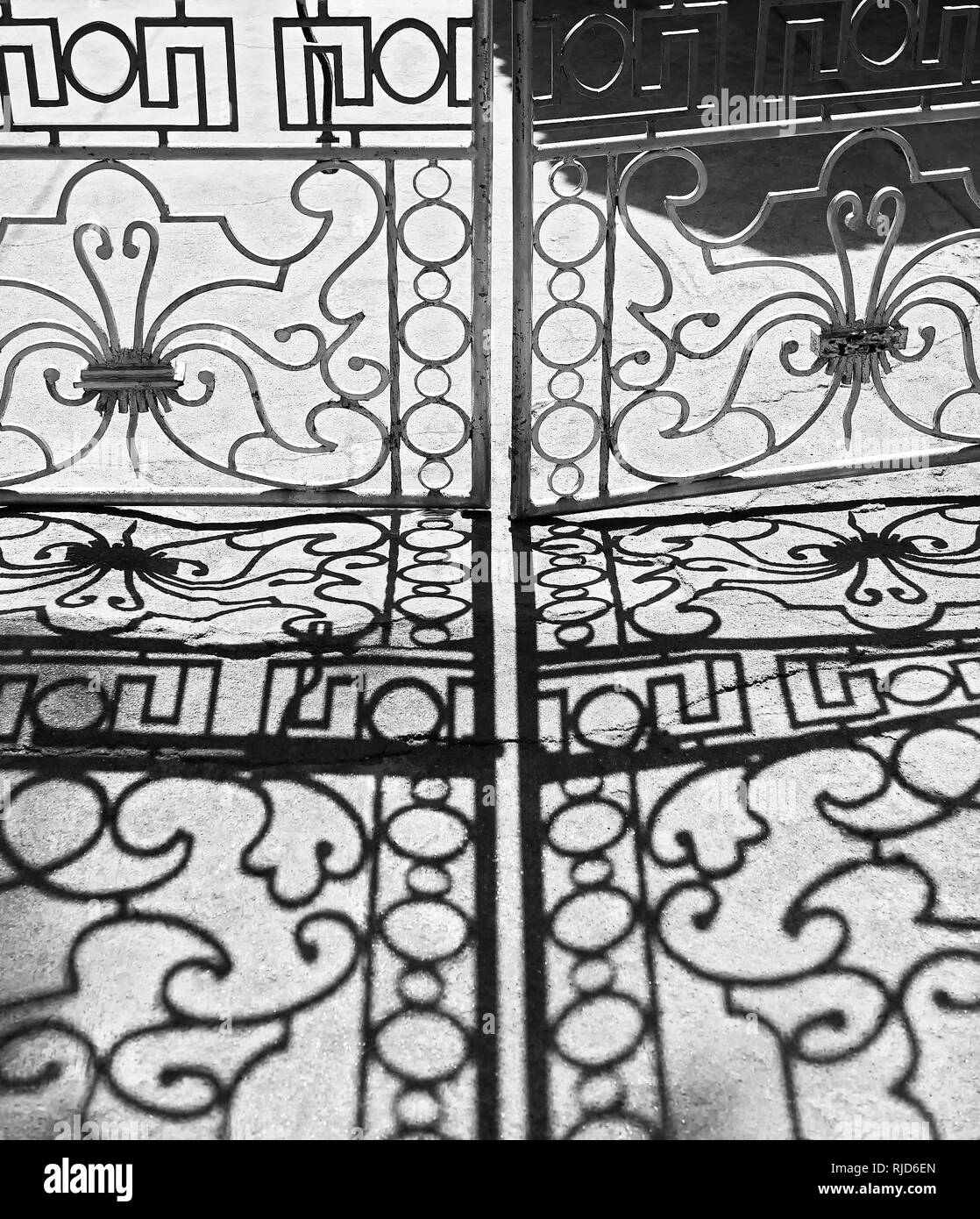 Closed iron crafted gate giving shadows on a grey floor, seen in Cuyo Town, Philippines. Photo is in black and white. Stock Photo