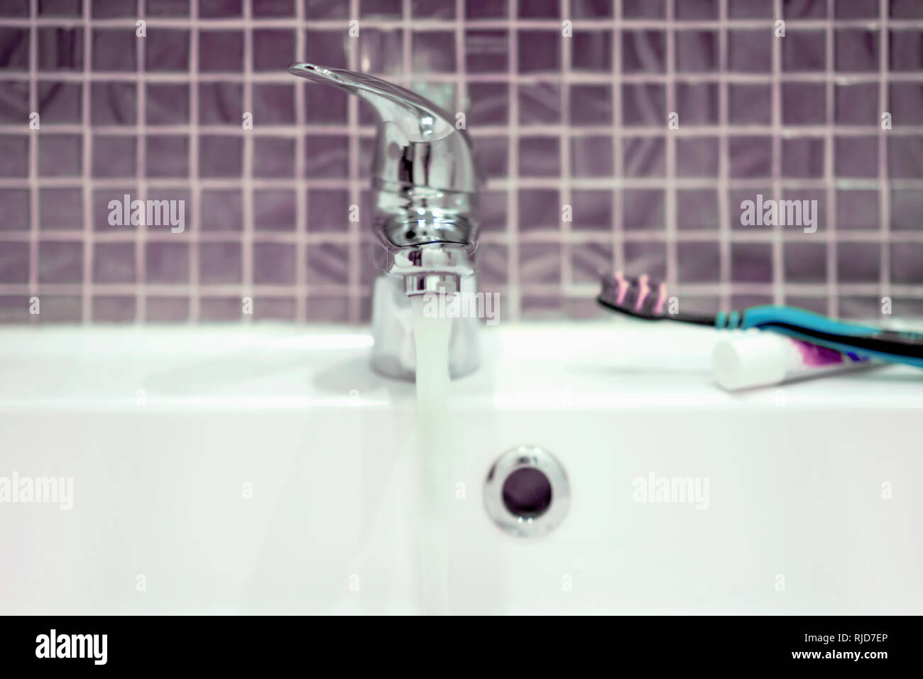 Sink and chrome faucet with flowing water in bathroom. Stock Photo