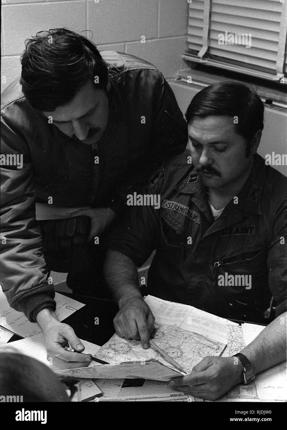Capt. Lawrence Hays (from left), Troop N, 107th Armored Cavalry, and Capt. Roy Stringham, 54th Support Center, plan flight operations from the Toledo Air National Guard base during the “Blizzard of ’78.” Ohio National Guard helicopter crews worked around the clock on medevac, rescue and resupply missions, averaging more than 200 flights a day during the peak period. (Ohio Army National Guard Historical Collections) Stock Photo