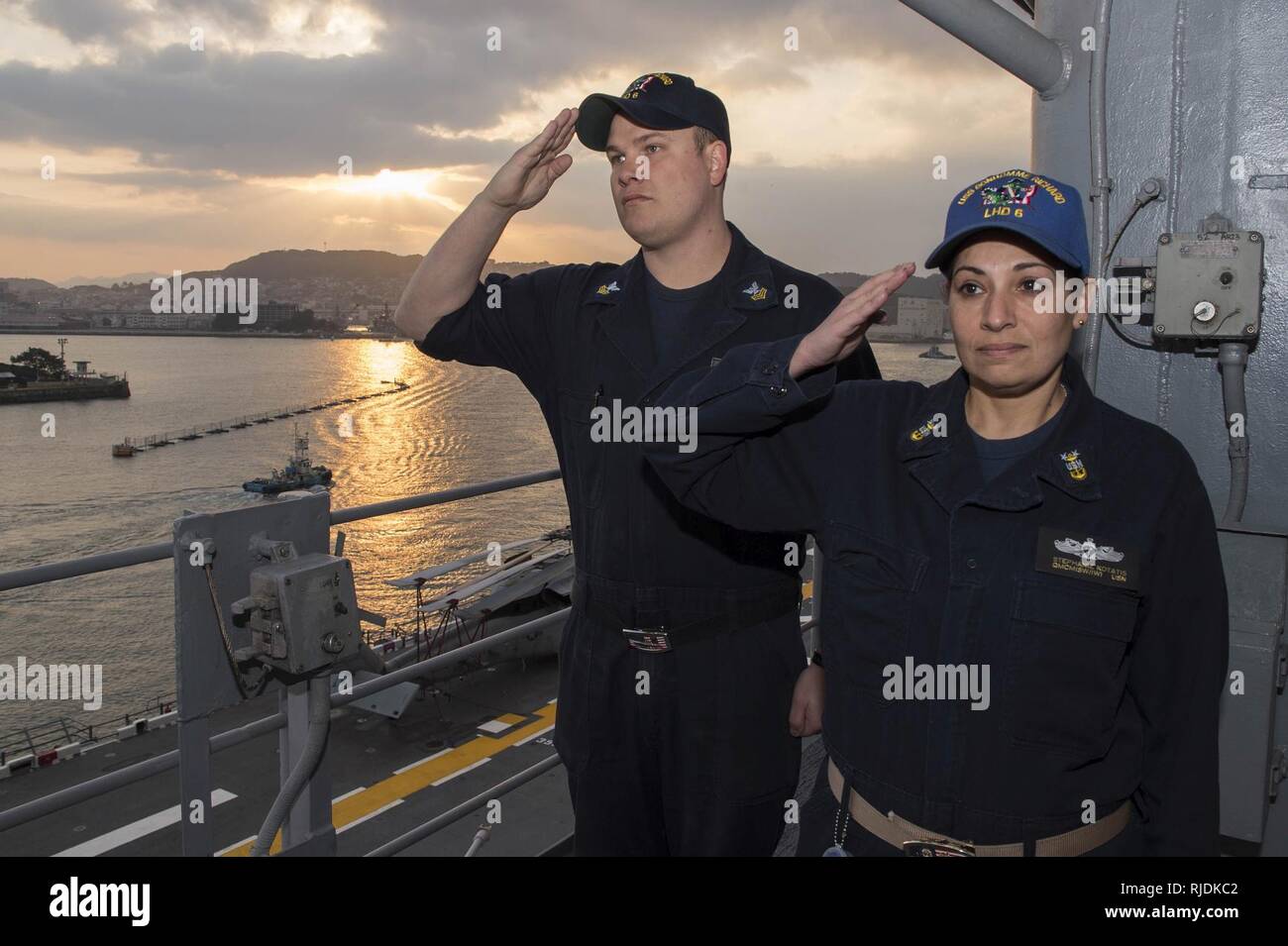 SASEBO, Japan (Jan. 23, 2018) Master Chief Quartermaster Stephanie Kortatis, right, from Sayreville, N.J., and Quartermaster 1st Class Matthew Lenerville, from Richardton, N.D., render honors during morning colors aboard the amphibious assault ship USS Bonhomme Richard (LHD 6) prior to the ship’s departure from Sasebo, Japan. Bonhomme Richard is underway conducting a Readiness for Sea assessment ahead of a regularly scheduled patrol in the Indo-Asia-Pacific region. Stock Photo
