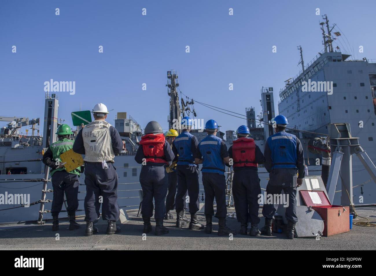 ARABIAN GULF (Jan. 10, 2018) Sailors observe a refueling hose traveling from the USNS Alan Shepard (T-AKE 3) to the Arleigh Burke-class guided-missile destroyer USS Preble (DDG 88) during a replenishment-at-sea. Preble is deployed with the Theodore Roosevelt Carrier Strike Group to the U.S. 5th Fleet area of operations in support of maritime security operations to reassure allies and partners and preserve the freedom of navigation and the free flow of commerce in the region. Stock Photo