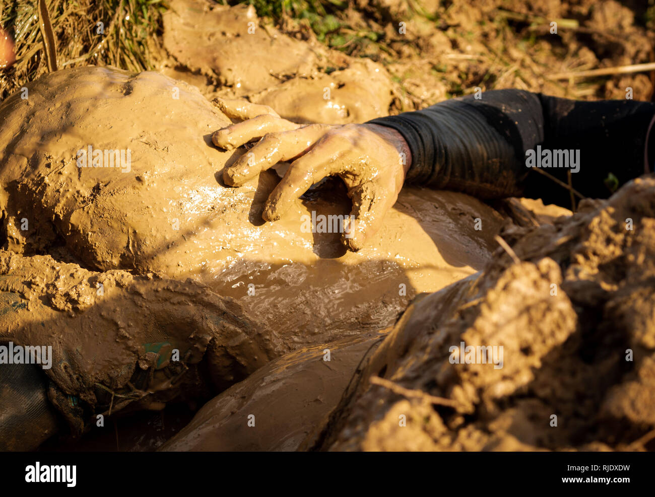 Muddy obstacle race runner in action. Mud run. Details of the hands. Stock Photo