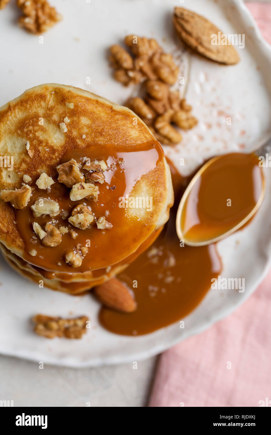 Close-up stack of american pancakes with caramel souse and nuts with spoon at plate. Macro. Concept of breakfast for kids. Top view Stock Photo
