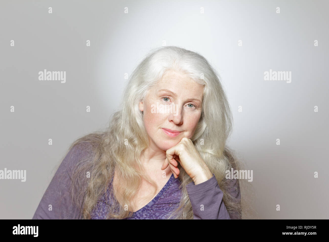 Headshot of a mature woman with beautiful curly long gray hair in front of white background, copy space. Stock Photo