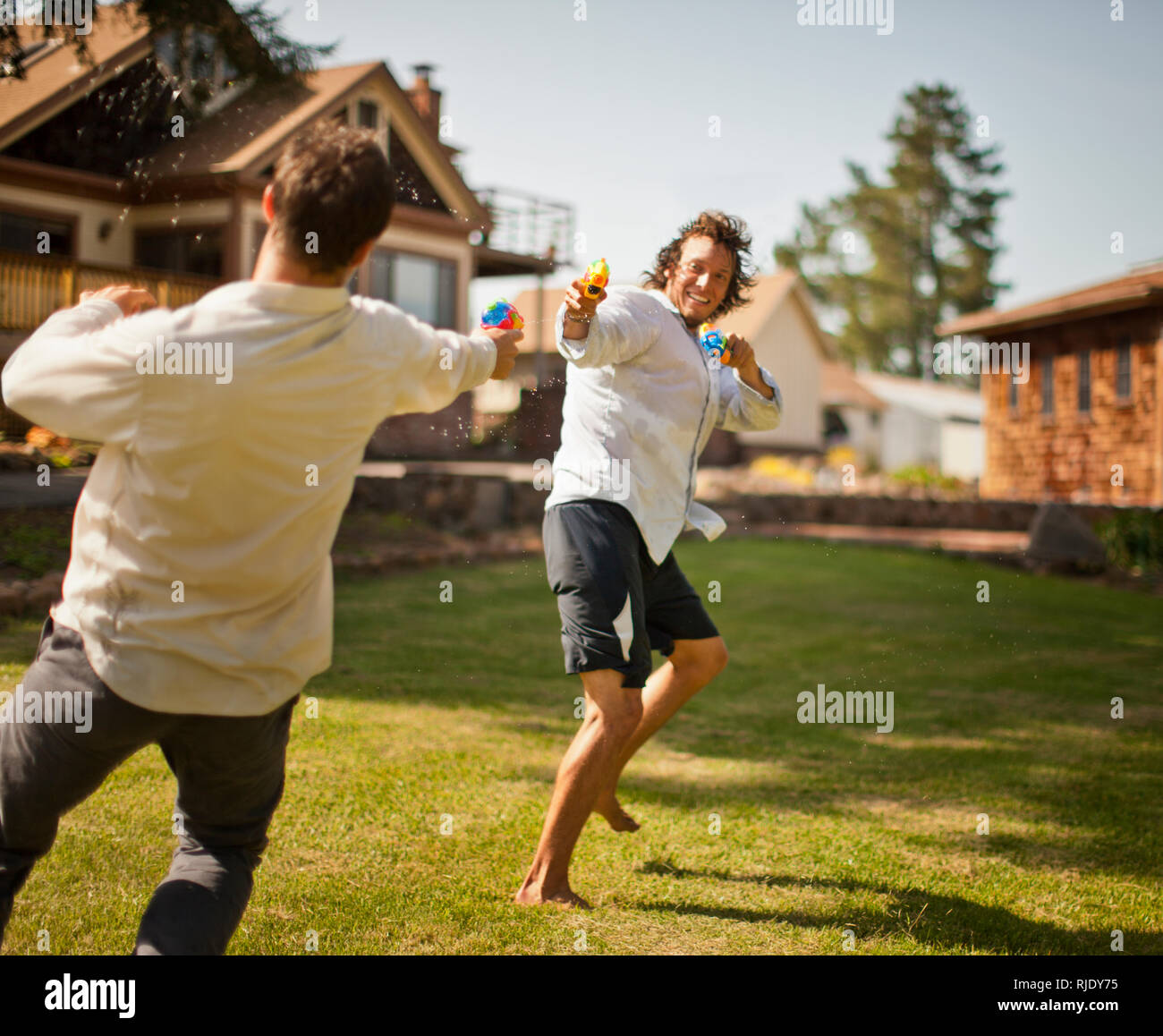 Two men having a water gun fight in a backyard. Stock Photo