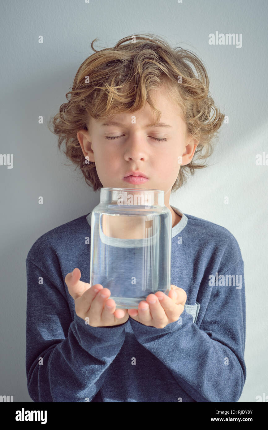 Sweet little boy keeping eyes closed and holding glass vase with