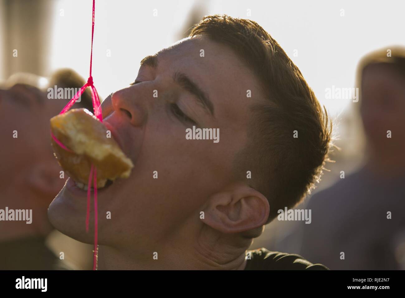 U.S. Marine Corps Flight Line Mechanic Lance Cpl. Shay Valdivieso, assigned to the Search and Rescue Unit with Headquarters & Headquarters Squadron (H&HS) at Marine Corps Air Station Yuma, Ariz., participates in the Donut Challenge, where Marines had to eat a pastry without using their hands during the H&HS Barracks Bash at Ramada Field Jan. 18, 2018. H&HS leadership and the station Single Marine Program coordinated the event to boost morale through fun, friendly competition. (Lance Cpl. Sabrina Candiaflores) Stock Photo