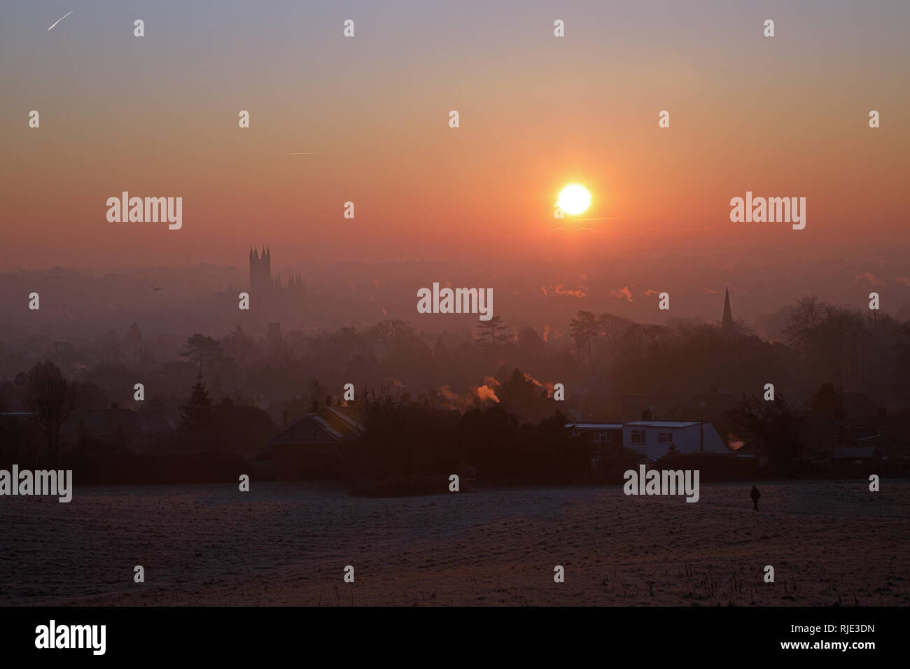 Sunrise over Canterbury on a cold, crisp January morning with aircraft vapour trails in the sky and a lone walker in the foreground. Stock Photo