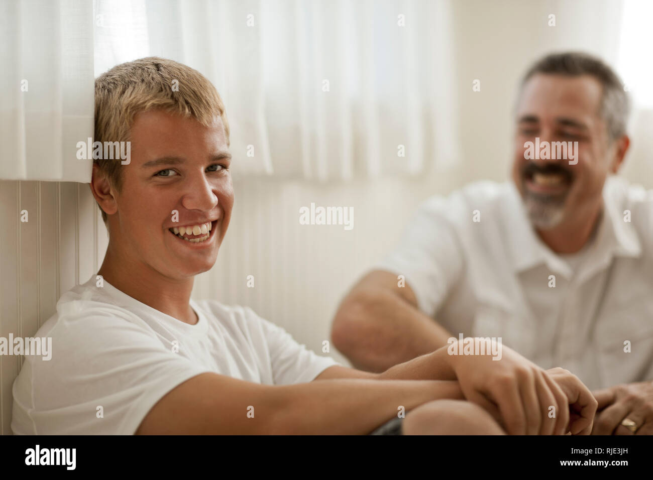 Portrait of a smiling teenage boy and mature adult man sitting together. Stock Photo