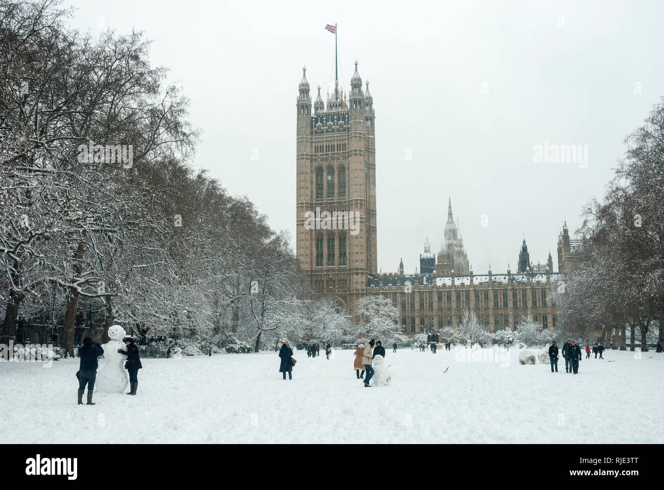 The Victoria Tower with Union Jack flying and Victoria Tower Gardens covered in snow and people walking and building snowmen. Stock Photo