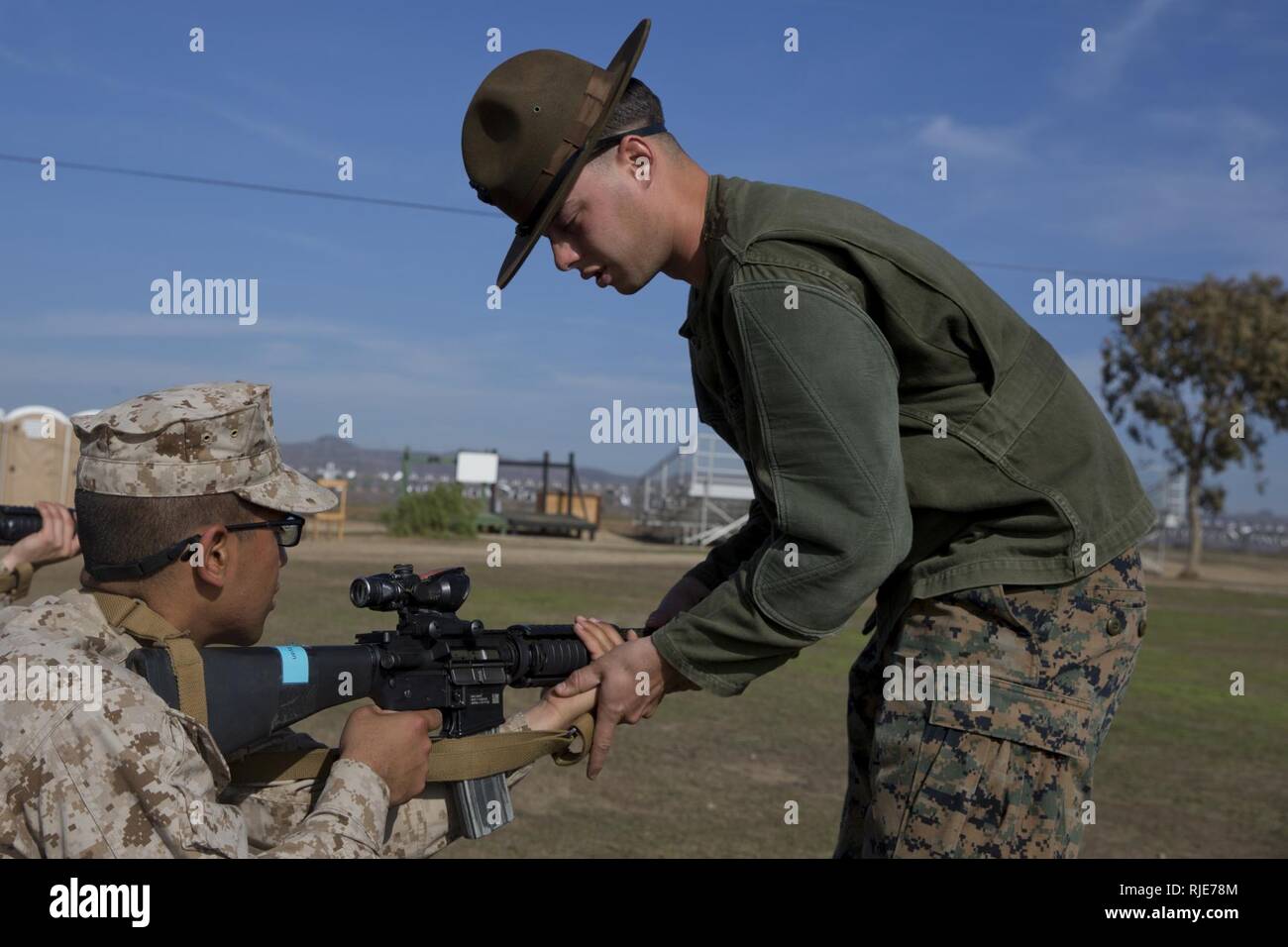 A primary marksmanship instructor, Edson Range, Weapons and Field Training Battalion, assists a recruit from Mike Company, 3rd Recruit Training Battalion, with his sitting position during grass week at Marine Corps Base Camp Pendleton, Calif., Jan. 17. The PMIs corrected the recruits’ shooting positions to improve their ability to accurately fire their weapons for qualification. Annually, more than 17,000 males recruited from the Western Recruiting Region are trained at MCRD San Diego. Mike Company is scheduled to graduate Feb. 23. Stock Photo