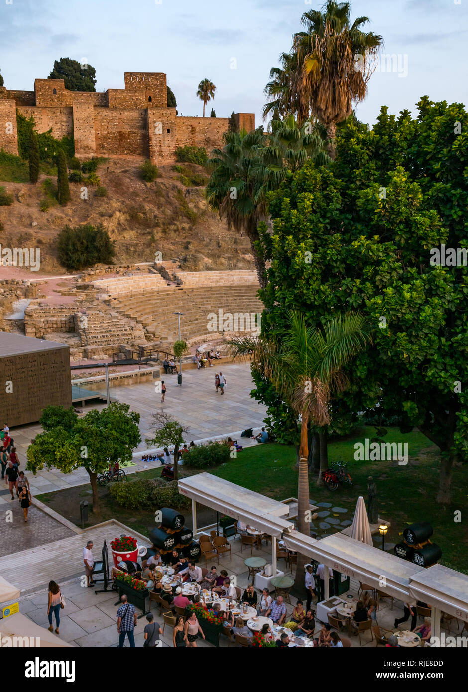 Alcazaba fortified walls and Roman Theatre at dusk with people eating at outdoor pavement tables, Malaga, Andalusia, Spain Stock Photo