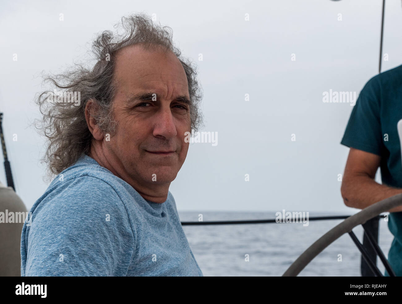 Older man sitting on a sailboat smiling off the coast of Lesvos Stock Photo
