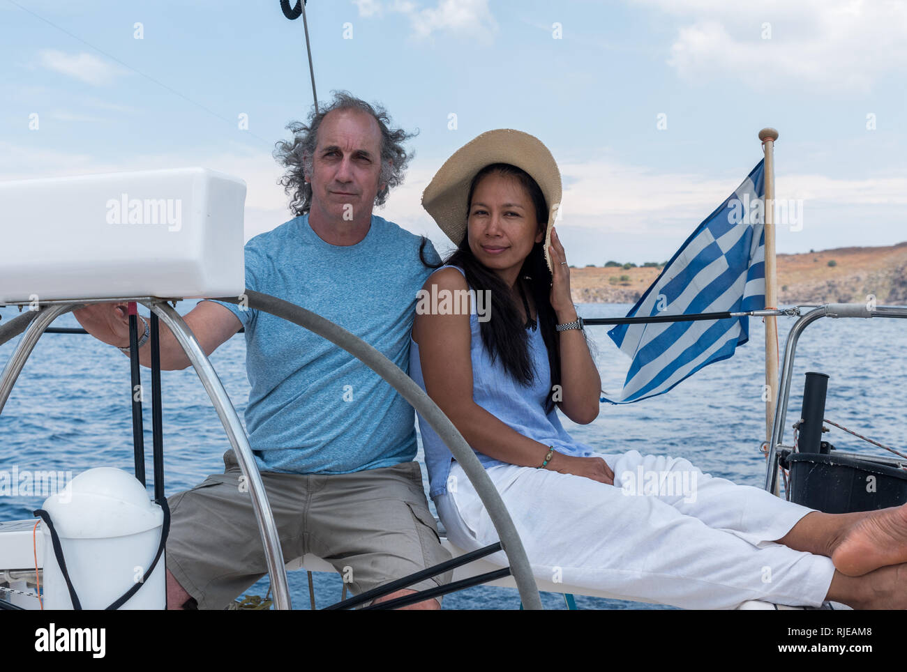 Man and woman with hat  in cockpit of sailboat with Greek flag Stock Photo