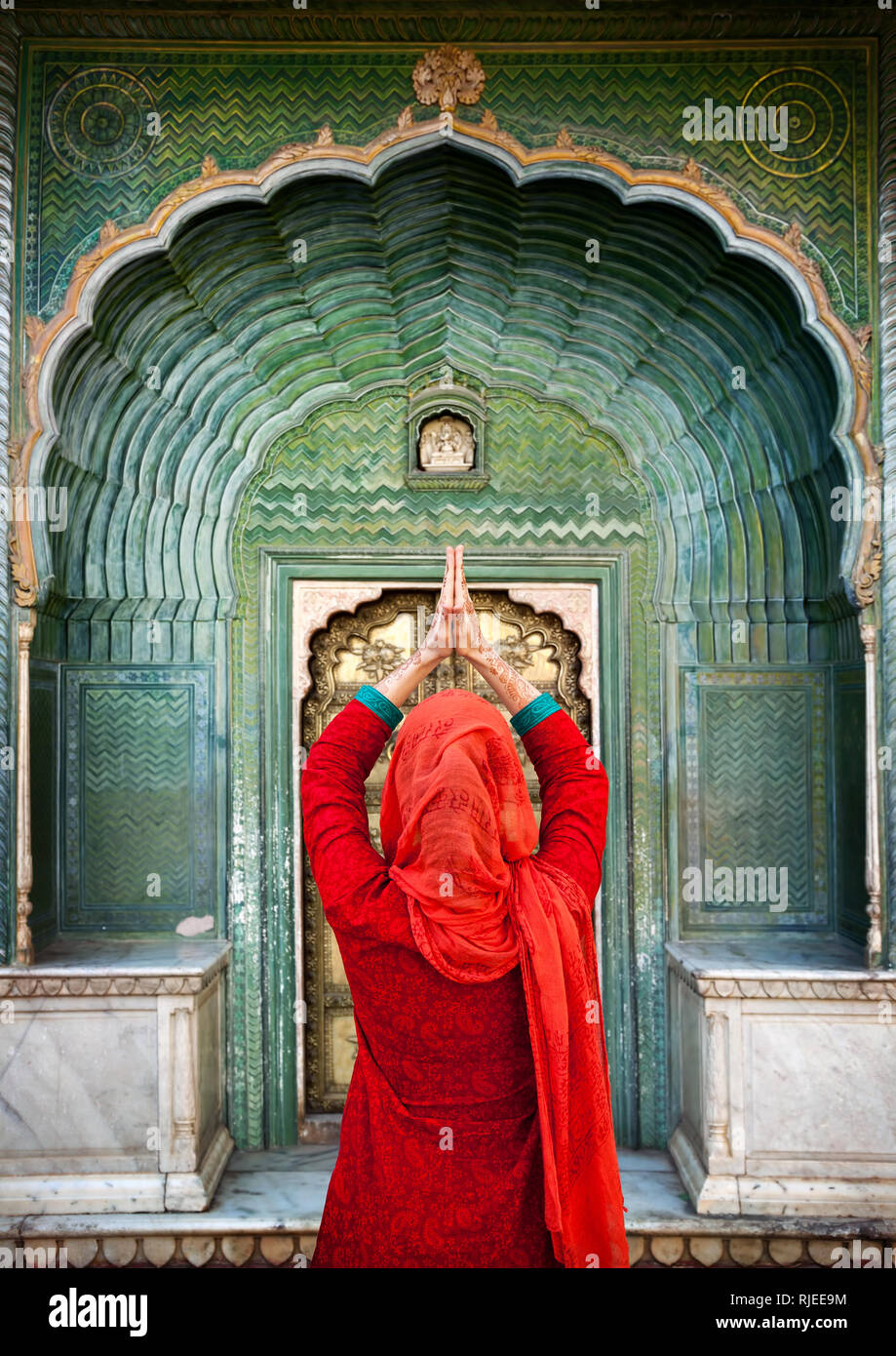 Indian Woman in red scarf with hands in prayer gesture at green gate door in City Palace of Jaipur, Rajasthan, India. Space for your text, can be used Stock Photo