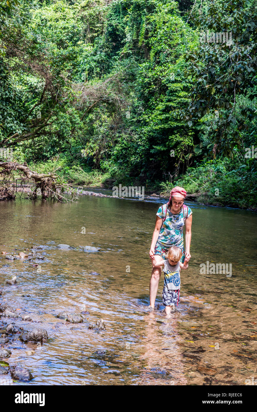 A nice photo of a mother and her child walking hand in hand in a shallow river in a beautiful tropical rain forest in Osa Peninsula, Costa Rica Stock Photo
