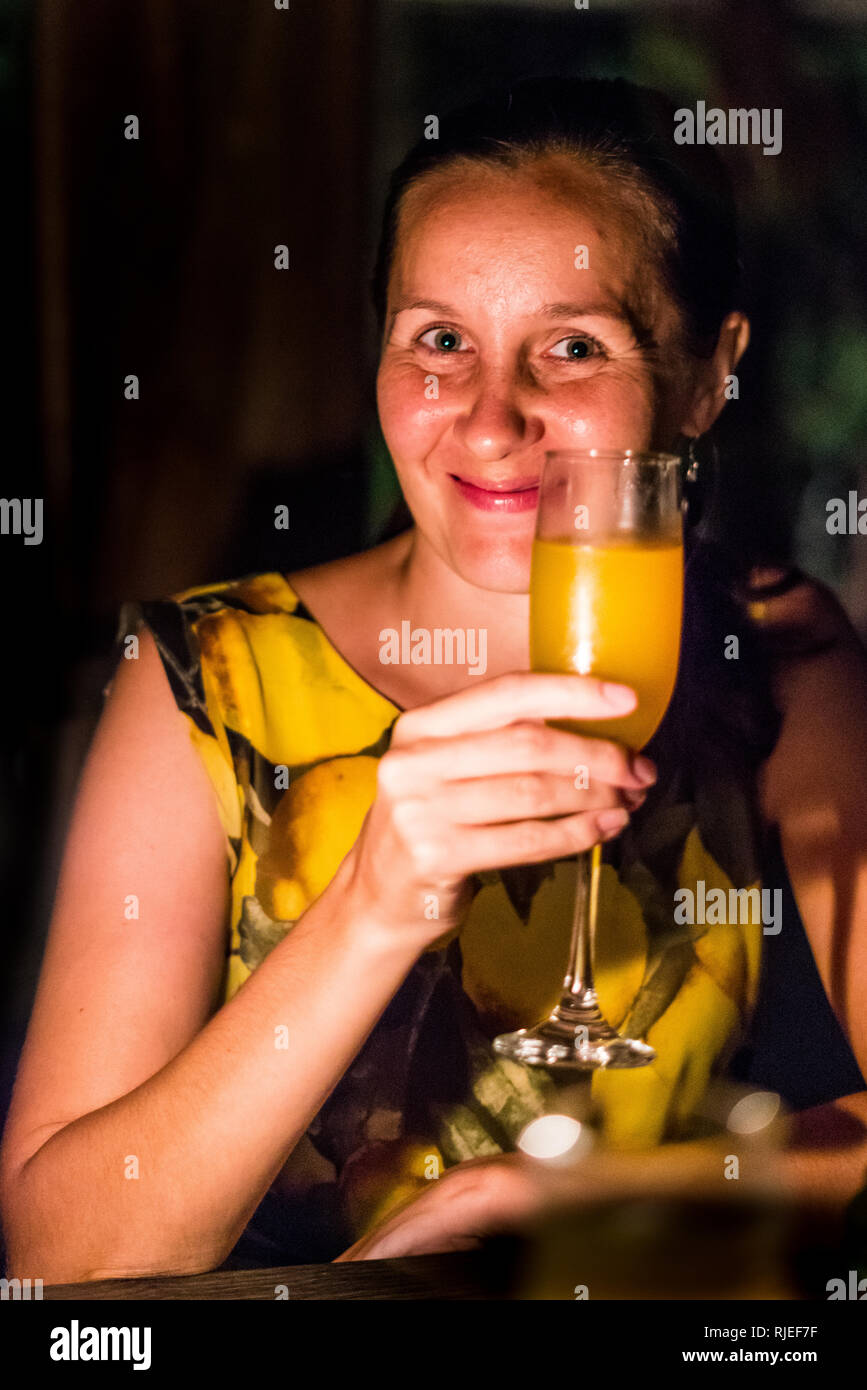 A nice portrait of a beautiful smiling woman in a yellow dress having a drink during a romantic dinner Stock Photo