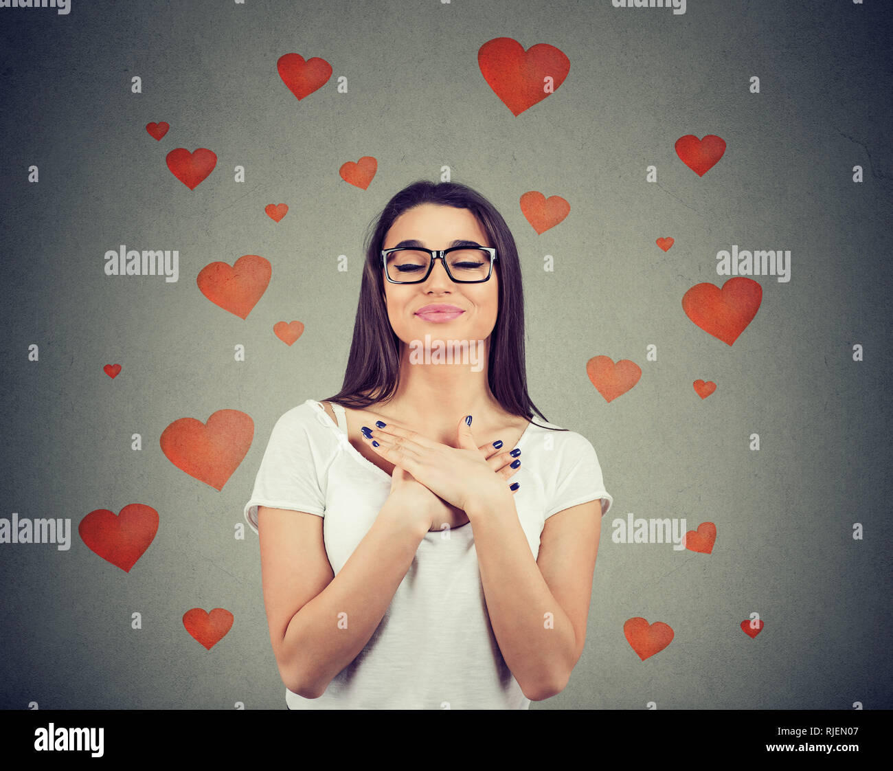 Woman in love with eyes closed keeps hands on chest near heart, shows kindness, expresses sincere emotions, being kind hearted. Stock Photo