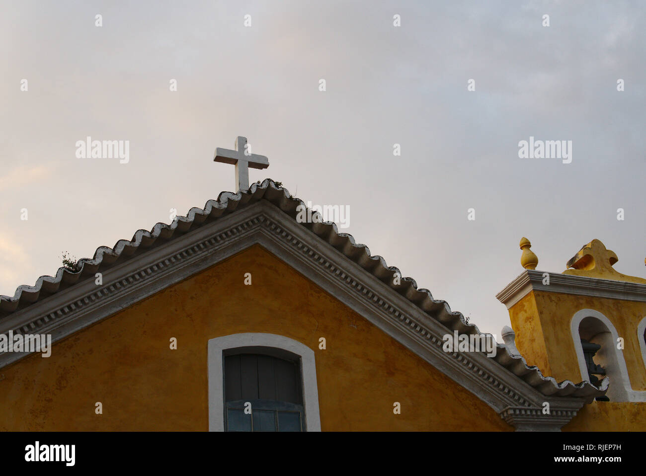 Top of a traditional Catholic church in America Latina. A yellow building with a white cross. Stock Photo
