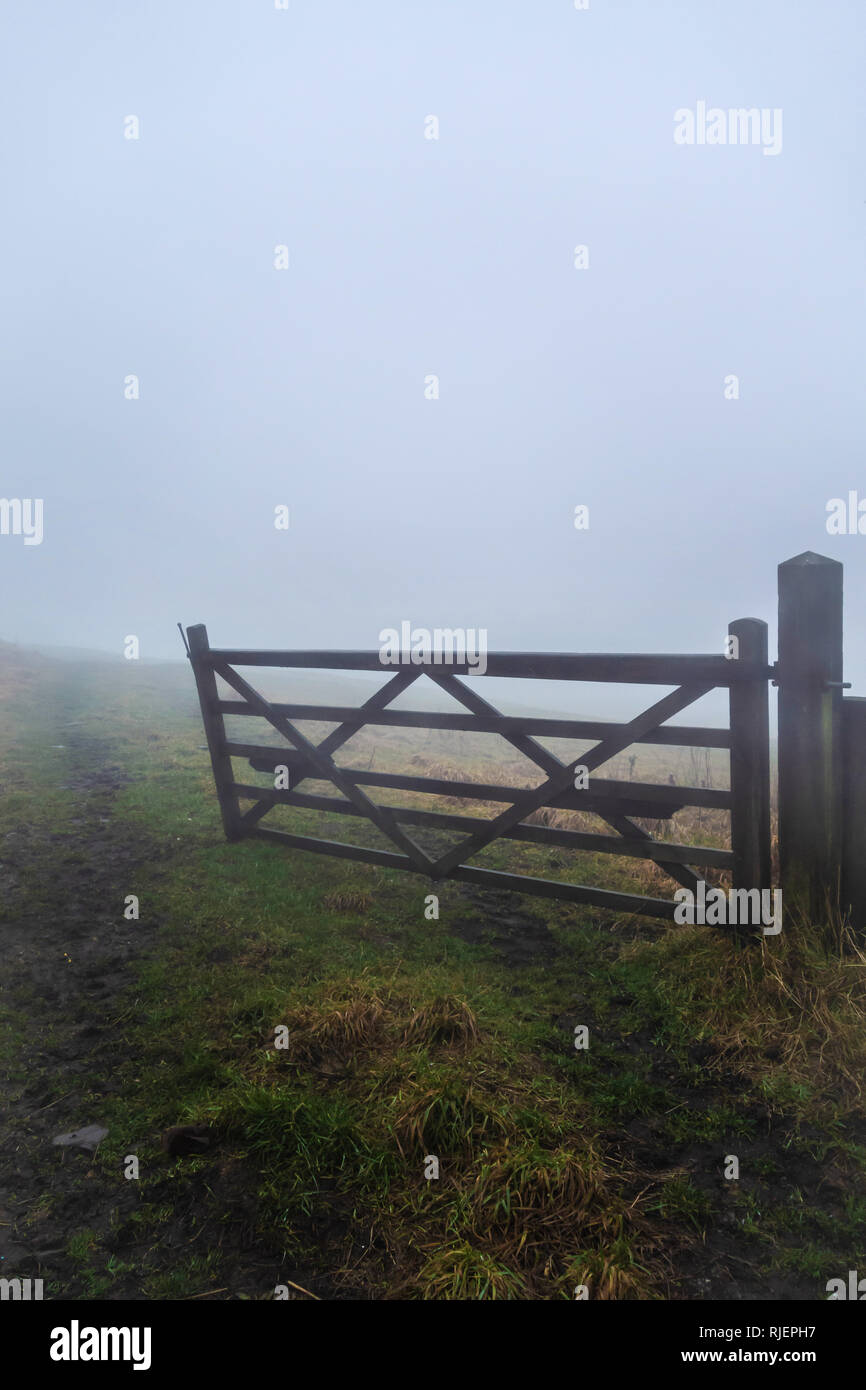 Part opened wooden farm gate leading to field seen on a winters foggy day in Lancashire, England Stock Photo