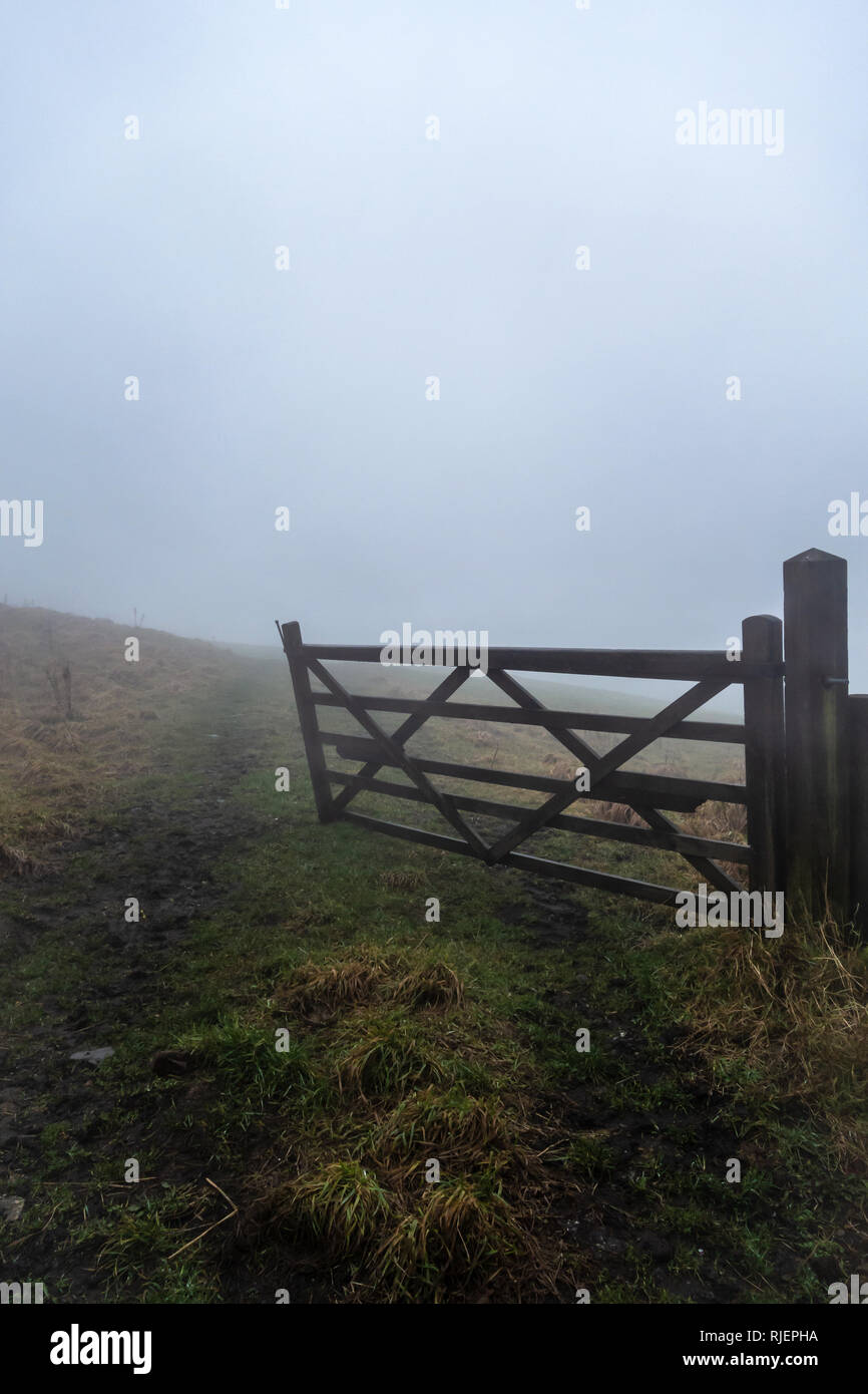 Part opened wooden farm gate leading to field seen on a winters foggy day in Lancashire, England Stock Photo